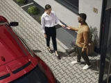 man en vrouw bij rode auto die autosleutel afgeven